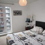 Cox & Co Estate agent in Edinburgh, Scotland. A bedroom with a bed featuring owl-patterned bedding, a black headboard, and a wall-mounted lamp above a small side table. There's a framed "FAMILY" photo collage on the wall, and a door with glass panels leading to a small balcony overlooking the buildings of Salamander Court.