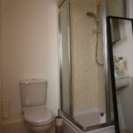 Cox & Co Estate agent in Edinburgh, Scotland. A small bathroom featuring a toilet, a sink with a soap dispenser on the right, and a glass-enclosed shower stall with a mirrored door. Next to the toilet is a roll of toilet paper. The white walls give the compact space a clean look, making it feel like your private court of tranquility.