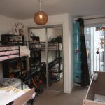 Cox & Co Estate agent in Edinburgh, Scotland. A cozy children's bedroom in Salamander Court features a bunk bed with a black metal frame, adorned with toys, and a wooden crib. A toy mobile hangs near the window, while a wardrobe with mirrored doors and a vertical blue storage unit complete this charming setup.