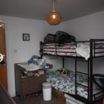 Cox & Co Estate agent in Edinburgh, Scotland. A child's room with bunk beds, a changing table, and a hanging mobile. The bunk beds have pastel-colored bedding, and baby items are spread on the changing table. A woven lamp hangs from the ceiling, shelves with toys and books are visible, and a plush salamander sits on one of the beds.
