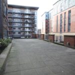 Cox & Co Estate agent in Edinburgh, Scotland. A paved courtyard, resembling a serene court, is surrounded by modern multi-story apartment buildings. A small garden bed containing plants on the left side adds a touch of nature. Each building has balconies, and the area appears to be quiet and clean.