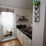 Cox & Co Estate agent in Edinburgh, Scotland. A compact kitchen with white cabinets and dark countertops. A window with a sheer curtain is in the background, letting in natural light. There is a small indoor garden with plants on the windowsill resembling a serene court. Kitchen appliances and utensils are neatly arranged.