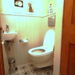 Cox & Co Estate agent in Edinburgh, Scotland. A small bathroom with a white toilet and a small sink. The floor has patterned tiles, and there is a roll of toilet paper on a holder next to the sink. Above the toilet, two framed pictures and a bottle of cleaning product rest on a shelf, adding charm that any estate agent in Edinburgh would appreciate.