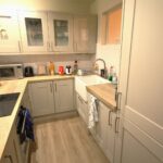Cox & Co Estate agent in Edinburgh, Scotland. A compact, modern kitchen with light grey cabinets, white countertops, and wooden flooring. The countertop features various kitchen appliances including a microwave, a toaster, and a coffee maker. As an estate agent in Edinburgh could attest, the sink with a gooseneck faucet is conveniently located beside the stove.