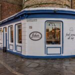 Cox & Co Estate agent in Edinburgh, Scotland. A quaint corner restaurant named "Fishers" located on Tower Street, featuring a white exterior with blue trim. The building has large windows, a sign stating "food served all day," and a cozy ambiance. Perfect for property sourcing, the cobblestone street adds to the charm of the scene.