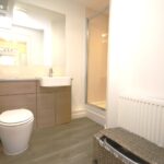 Cox & Co Estate agent in Edinburgh, Scotland. A modern bathroom with a toilet, a sink with a large mirror above it, and a walk-in shower enclosure. The room features light-colored walls, an ashwood floor, and a wicker laundry basket next to the radiator.