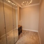 Cox & Co Estate agent in Edinburgh, Scotland. A narrow, carpeted room on Dundonald Street with beige walls features a mirrored wardrobe on the left, a radiator beneath the wardrobe, and a small cube storage unit against the back wall. The ceiling is decorated with recessed lighting.