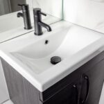 Cox & Co Estate agent in Edinburgh, Scotland. A modern bathroom sink with a white rectangular basin and a black faucet, located in a stylish flat on Piersfield Terrace, Edinburgh, EH8. The sink is mounted on a dark wood vanity with two handles. The wall behind the sink is tiled in white with a marble pattern, and a large mirror reflects the sink and faucet.