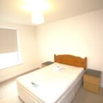 Cox & Co Estate agent in Edinburgh, Scotland. A simple, brightly lit bedroom with a double bed in the center, flanked by two bedside tables. The bed has a light wooden headboard and a clean mattress with folded linens on top. A chest of drawers stands near a window, creating a peaceful place to relax with the roller blind drawn down.