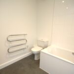 Cox & Co Estate agent in Edinburgh, Scotland. A modern bathroom with white walls and a grey floor features a white toilet and a white bathtub with a fitted screen on the right. A silver towel rail is mounted on the wall to the left of the toilet. The place appears clean and minimalist, providing a serene oasis amidst everyday life.