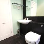 Cox & Co Estate agent in Edinburgh, Scotland. A modern bathroom featuring a white wall-mounted sink, black tiled walls, and floor. The sink has a chrome faucet and soap dispenser. Beneath a large mirror is a white toilet with a towel draped over the seat. A small garbage bin is placed beside the sink, bringing an air of terrace elegance to the space.