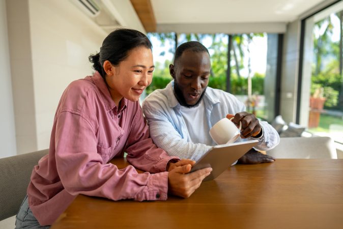 Happy multiethnic couple with laptop at home making plan for investments, savings and budget for bills. Online banking and financial payment with diverse, multiethnic husband and wife